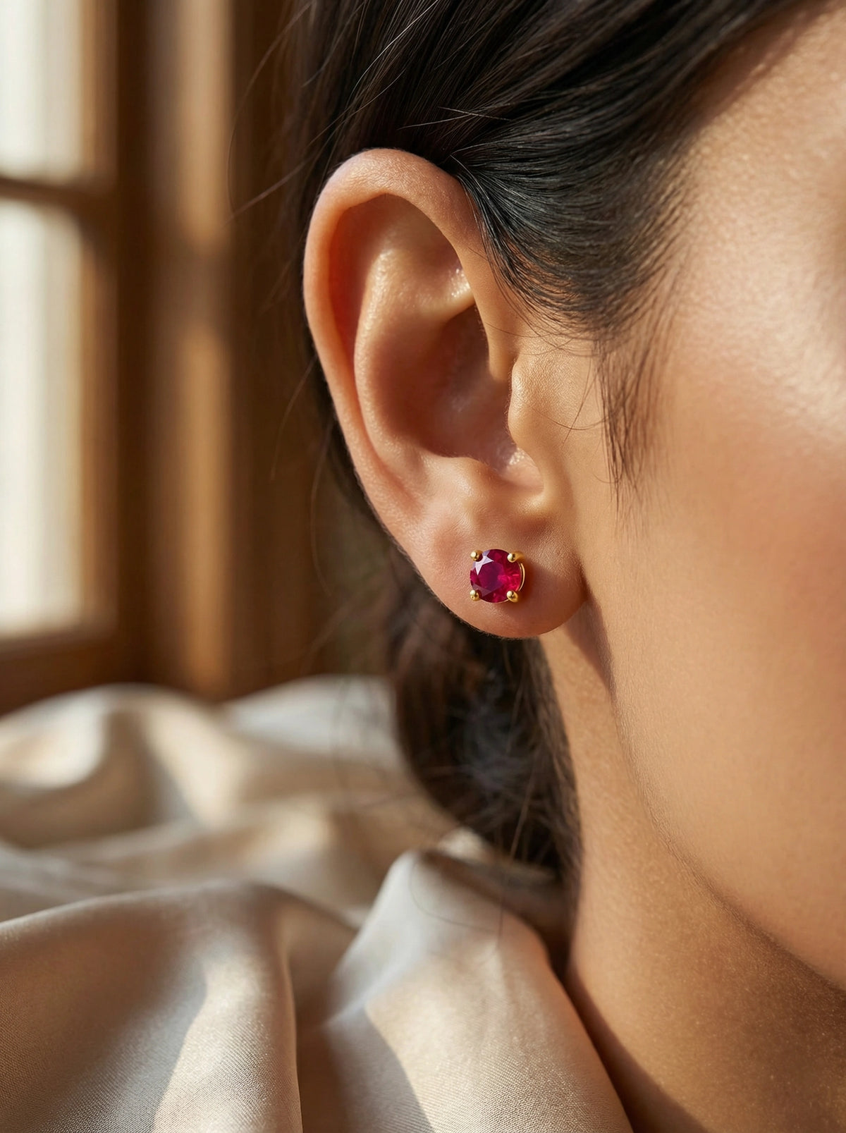 close-up of an ear wearing a 18k gold plated red gemstone earring with a soft background