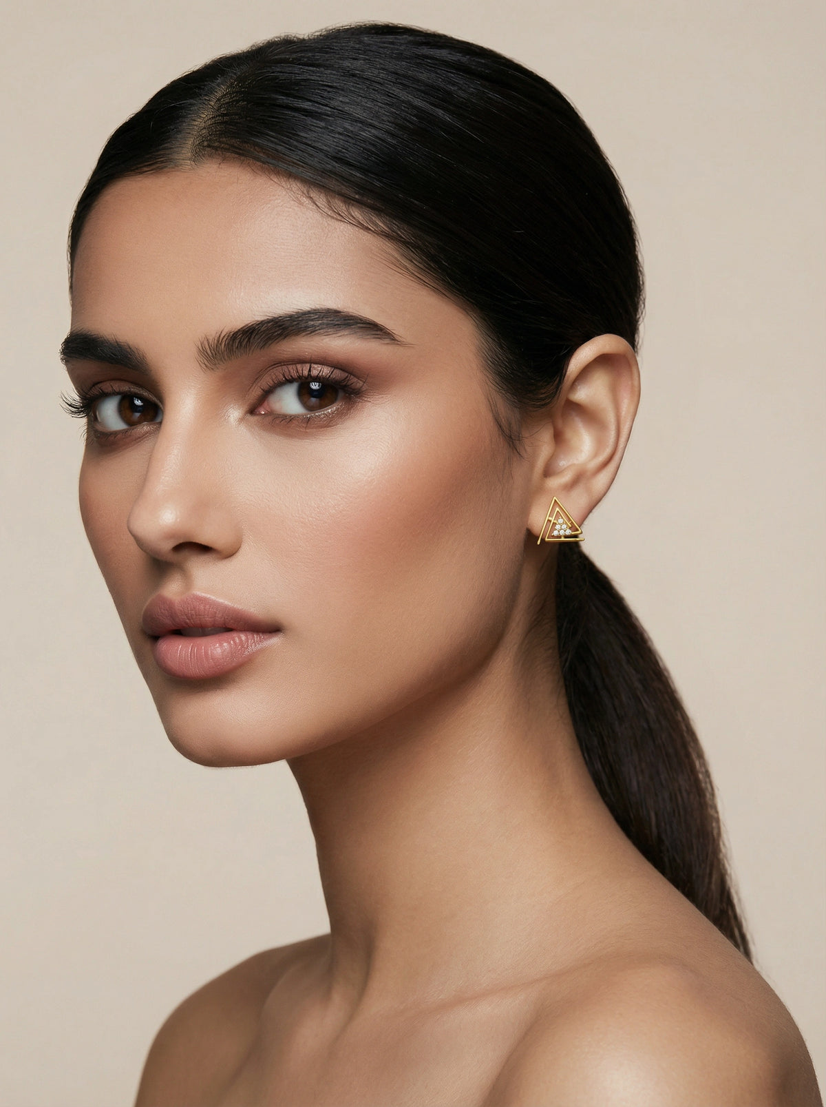 woman wearing a 18k gold plated triangle earring against a beige background