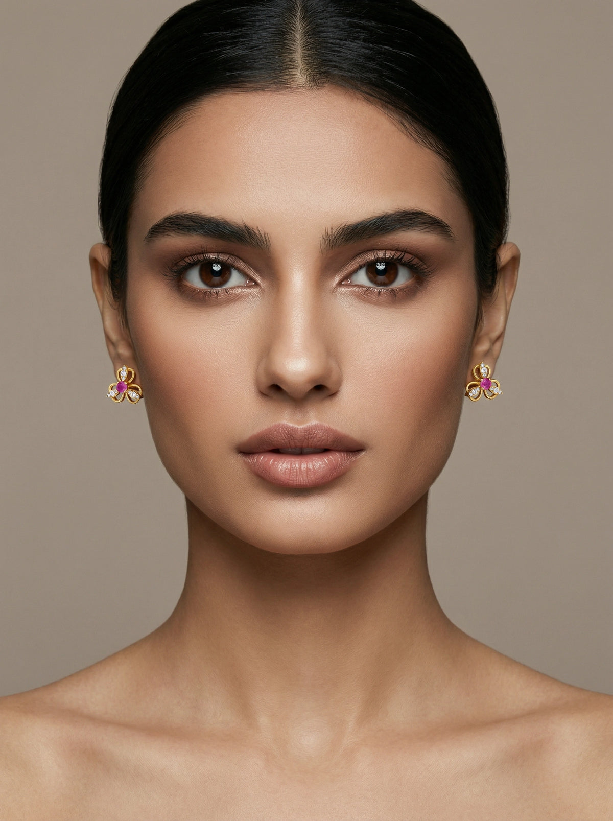 close-up of a woman wearing 18k gold plated earrings with pink stones against a beige background