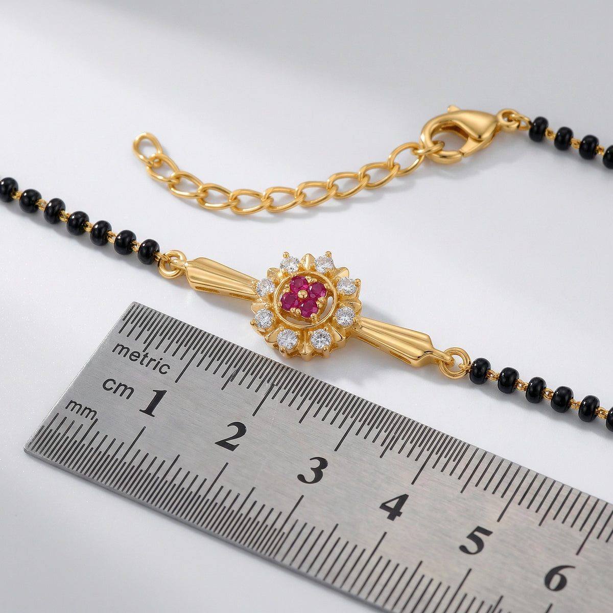 18k gold plated bracelet with a red gemstone next to a ruler on a white background