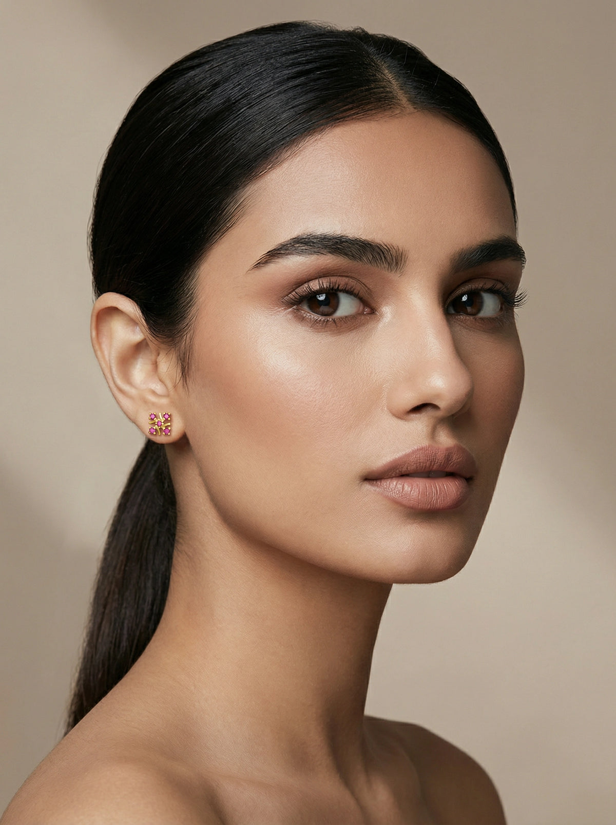woman with a sleek ponytail wearing 18k gold plated earrings against a neutral backgroundld 