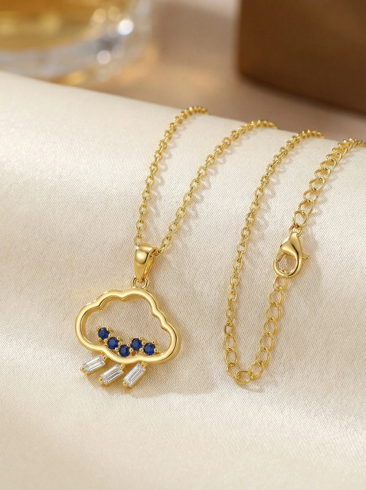 18k gold plated necklace with a cloud pendant featuring blue stones on a beige surface