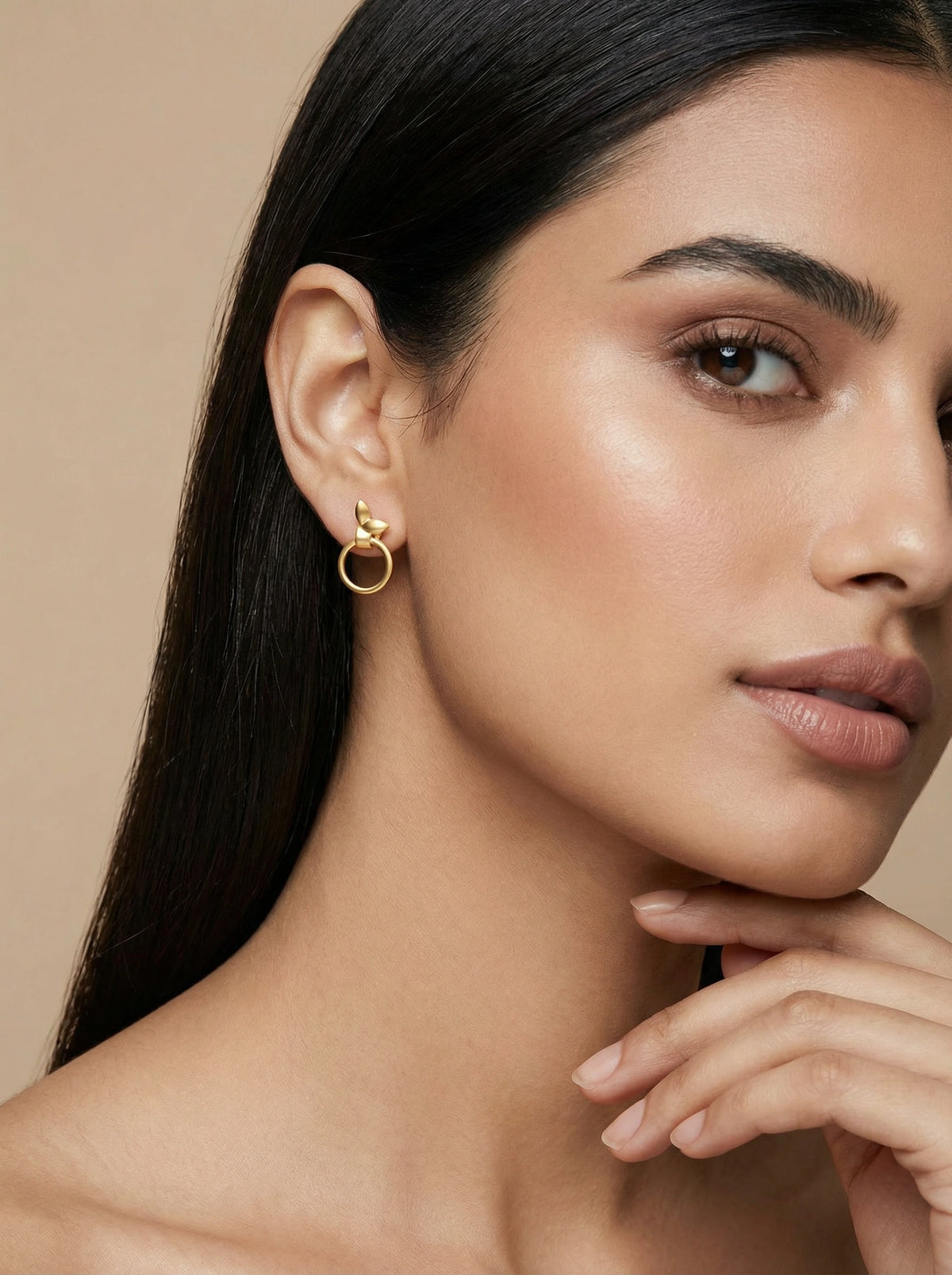 woman wearing a 18k gold plated earring against a beige background