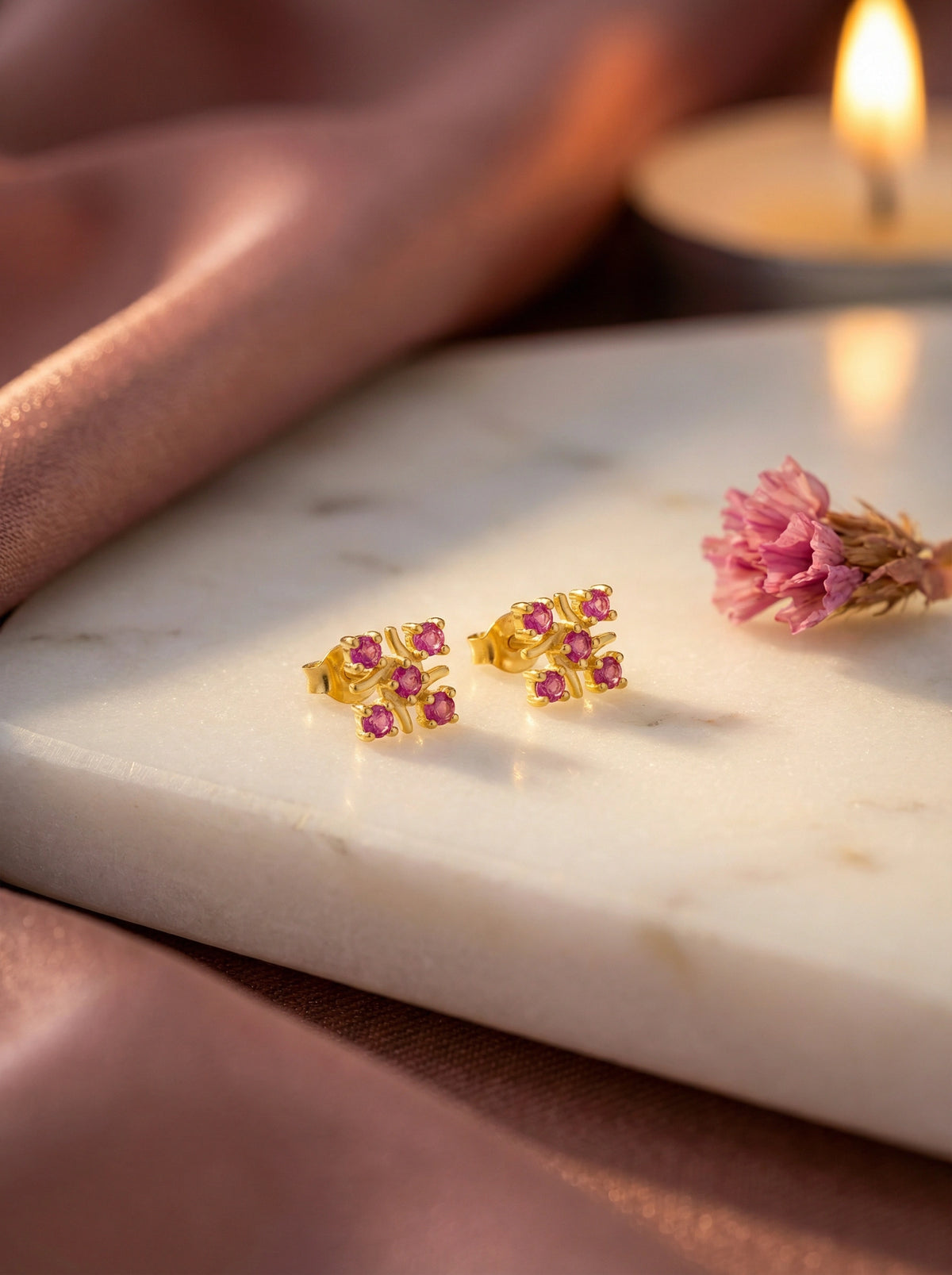 18k gold plated earrings with pink stones on a marble surface with a candle in the background