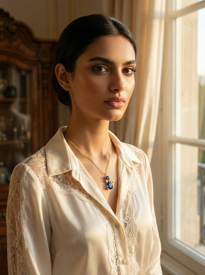 Woman wearing a white lace shirt with 18k gold plated  necklace, standing by a window.