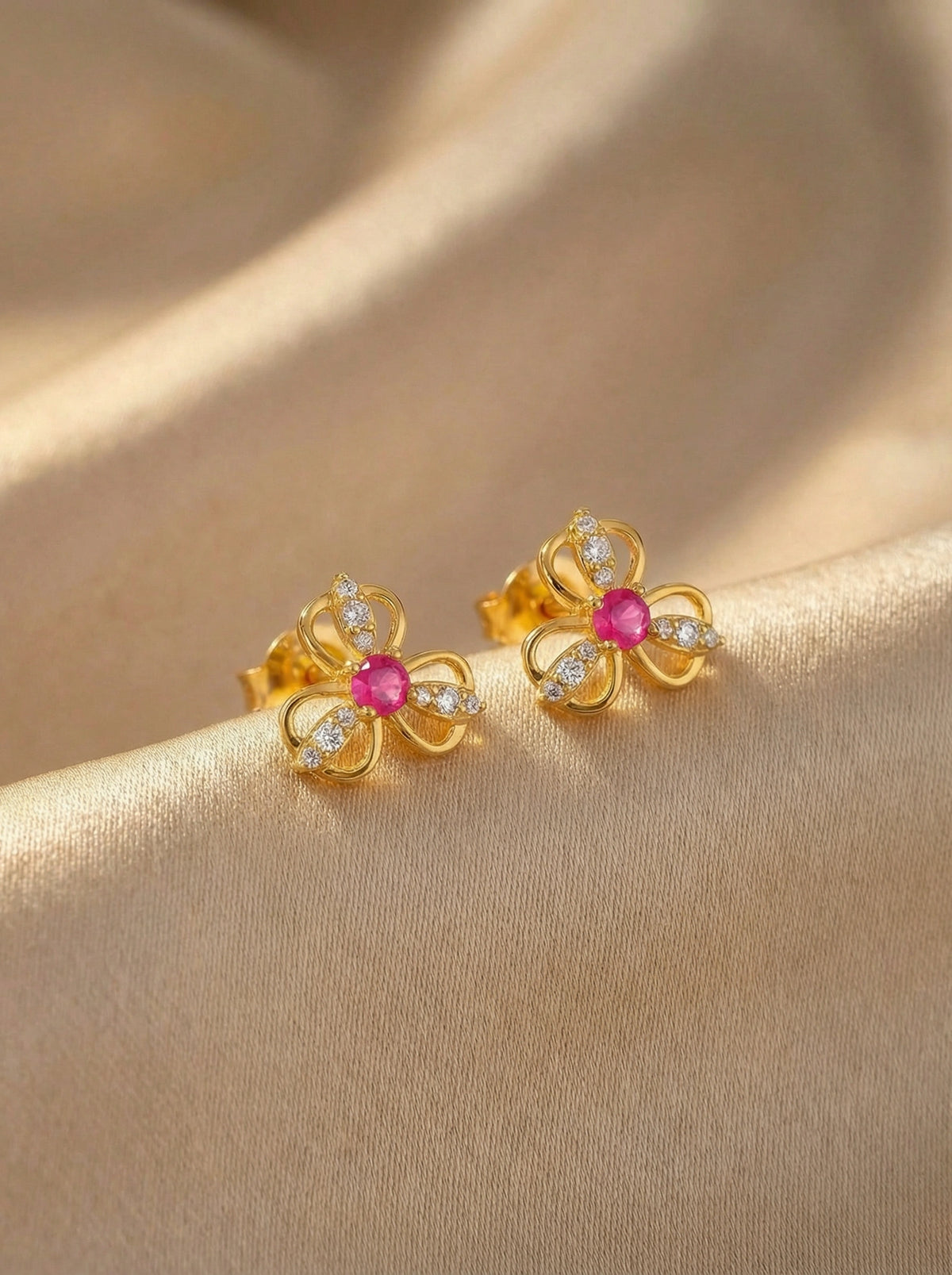 18k gold plated flower-shaped earrings with pink gemstones on a beige fabric background