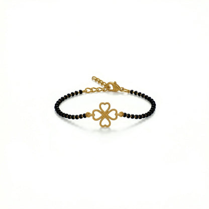 Gold bracelet with black beads and clover charm on a white background