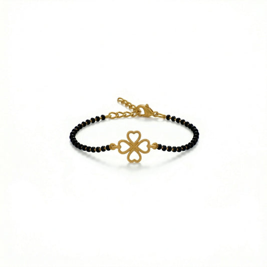 Gold bracelet with black beads and clover charm on a white background