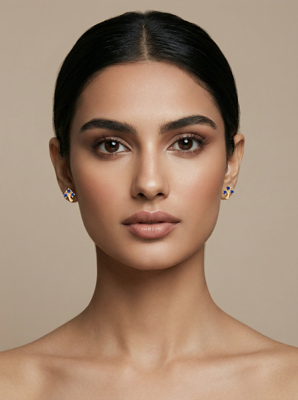 woman wearing 18k  gold plated earrings against a beige background