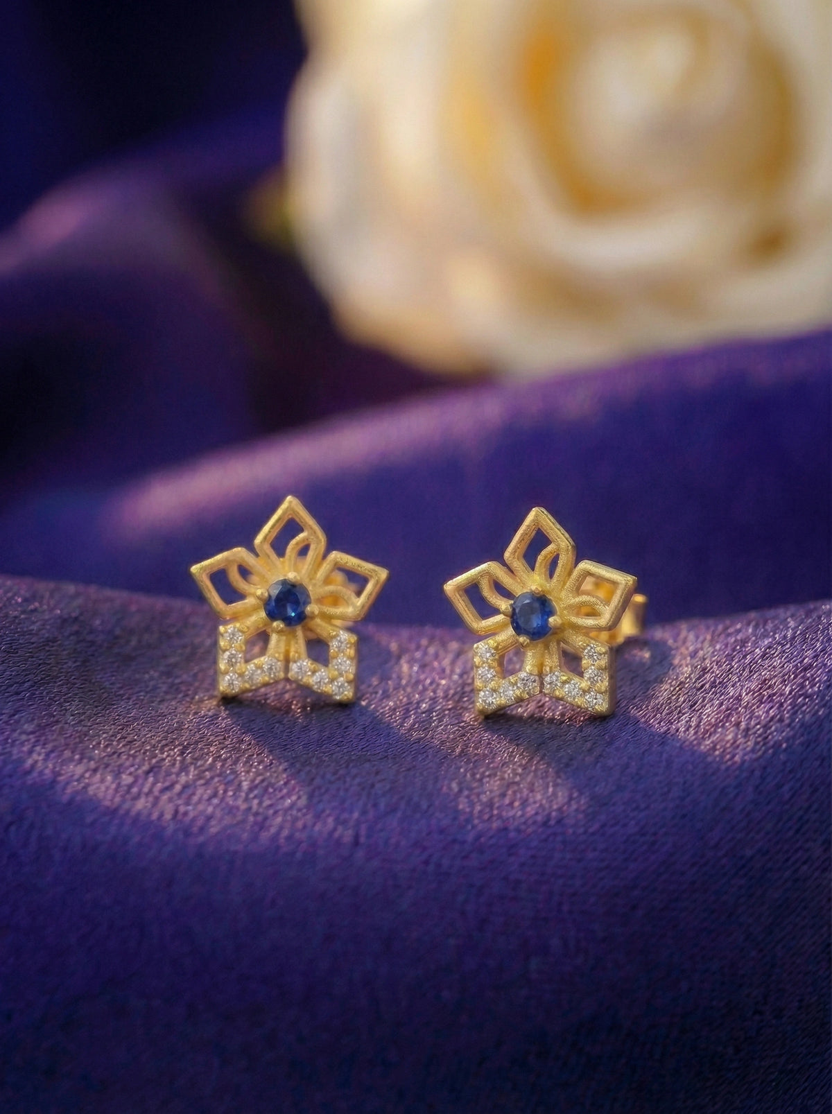 18k gold plated star-shaped earrings with blue stones on a purple fabric background