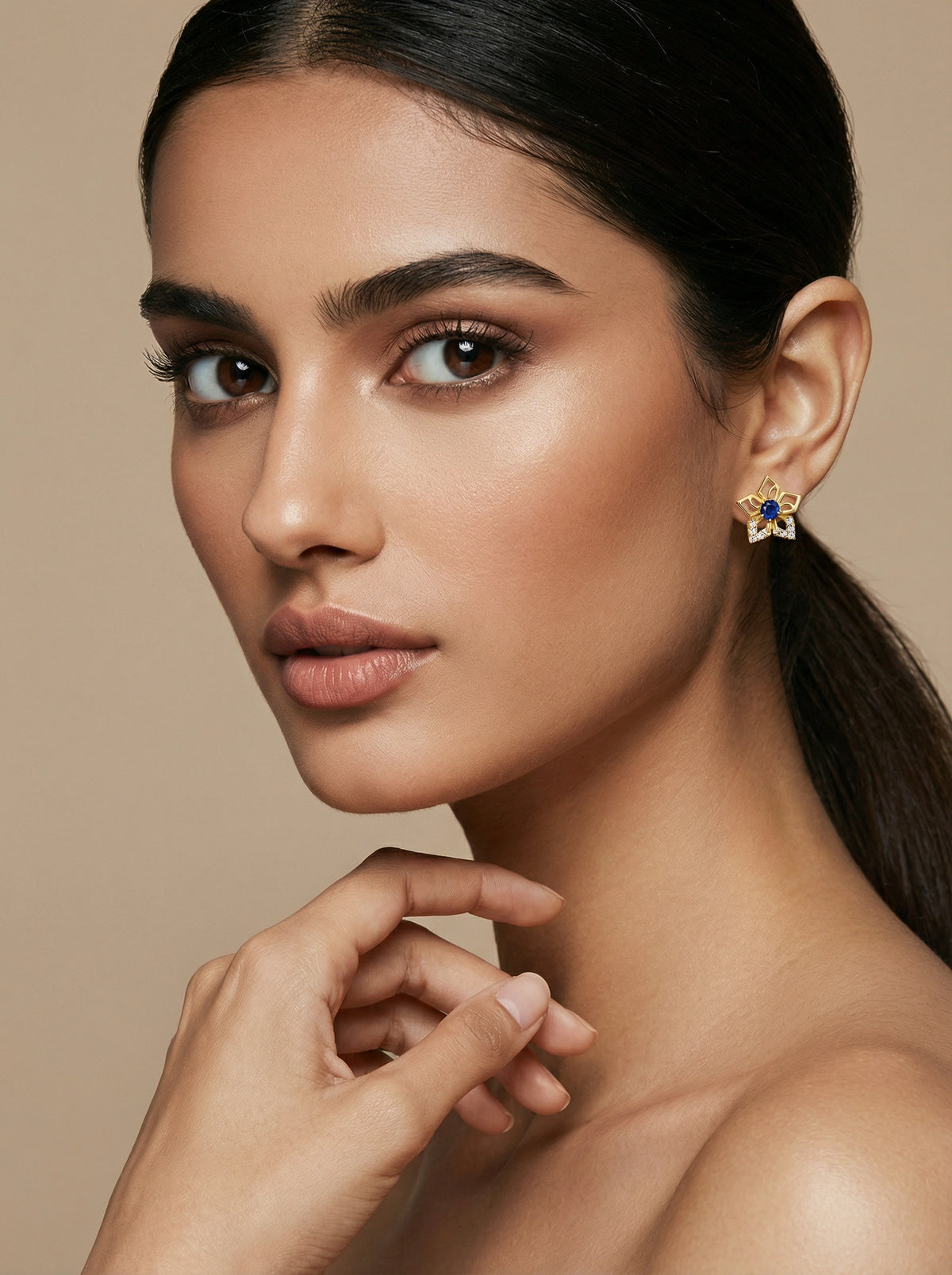close-up of a woman wearing a 18k gold plated earring with a blue gemstone on a beige background