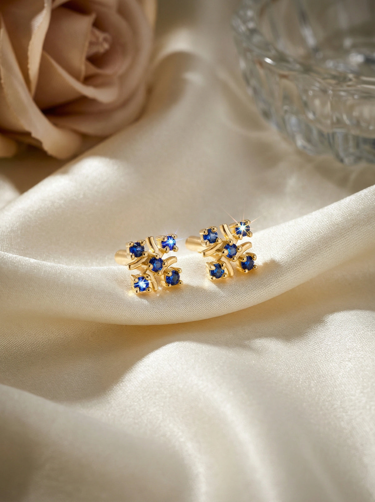 18k gold plated earrings with blue stones on a beige fabric background