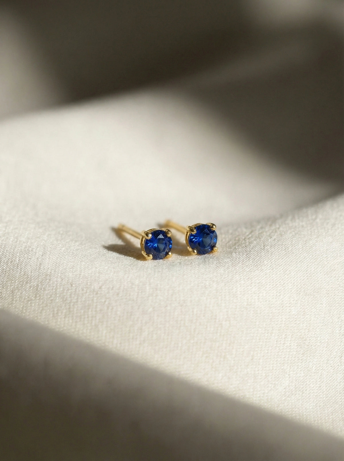 18k gold plated earrings with blue gemstones on a white fabric background