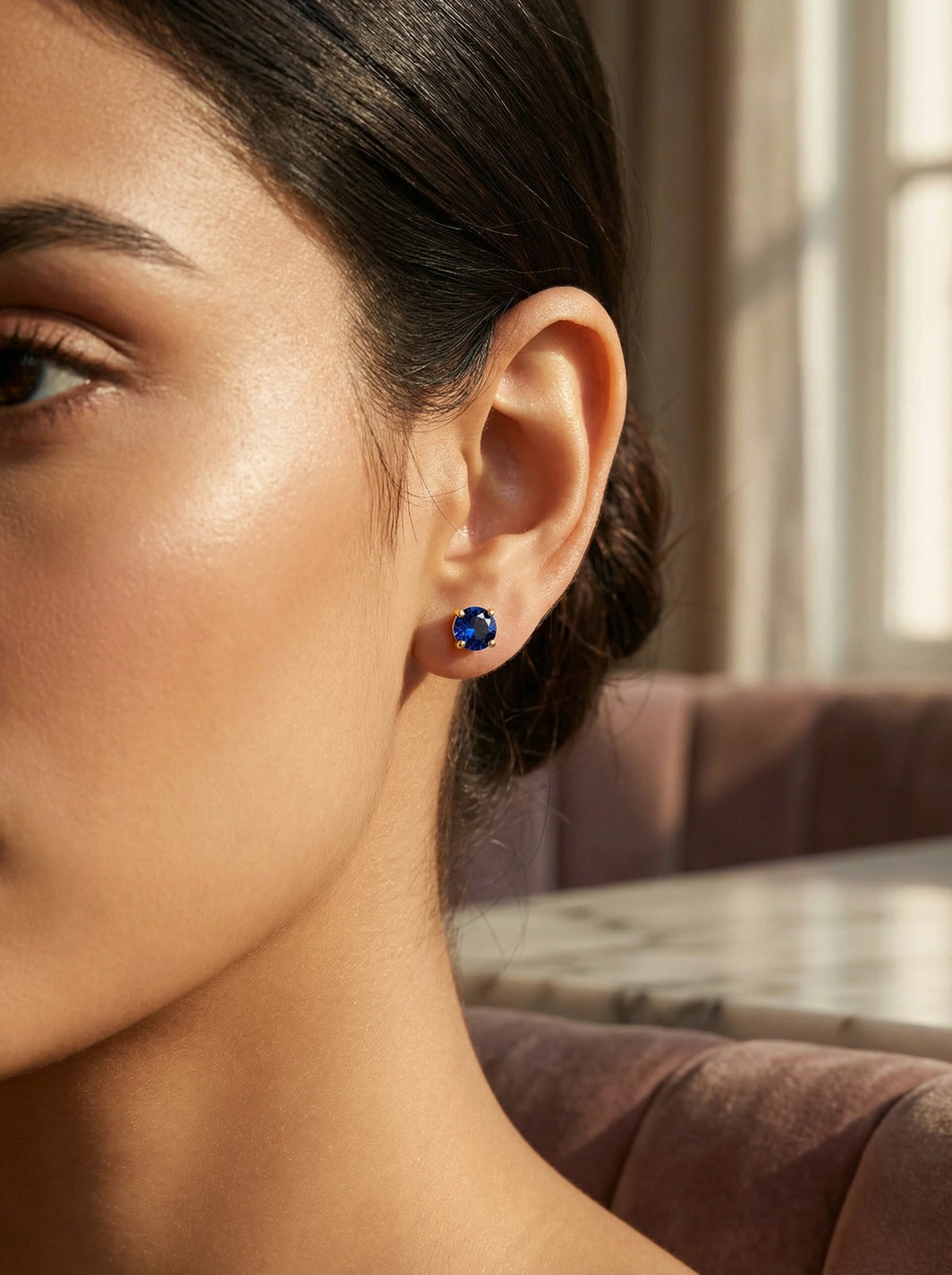 close-up of a woman wearing 18k  gold plated  blue gemstone earrings with a blurred background