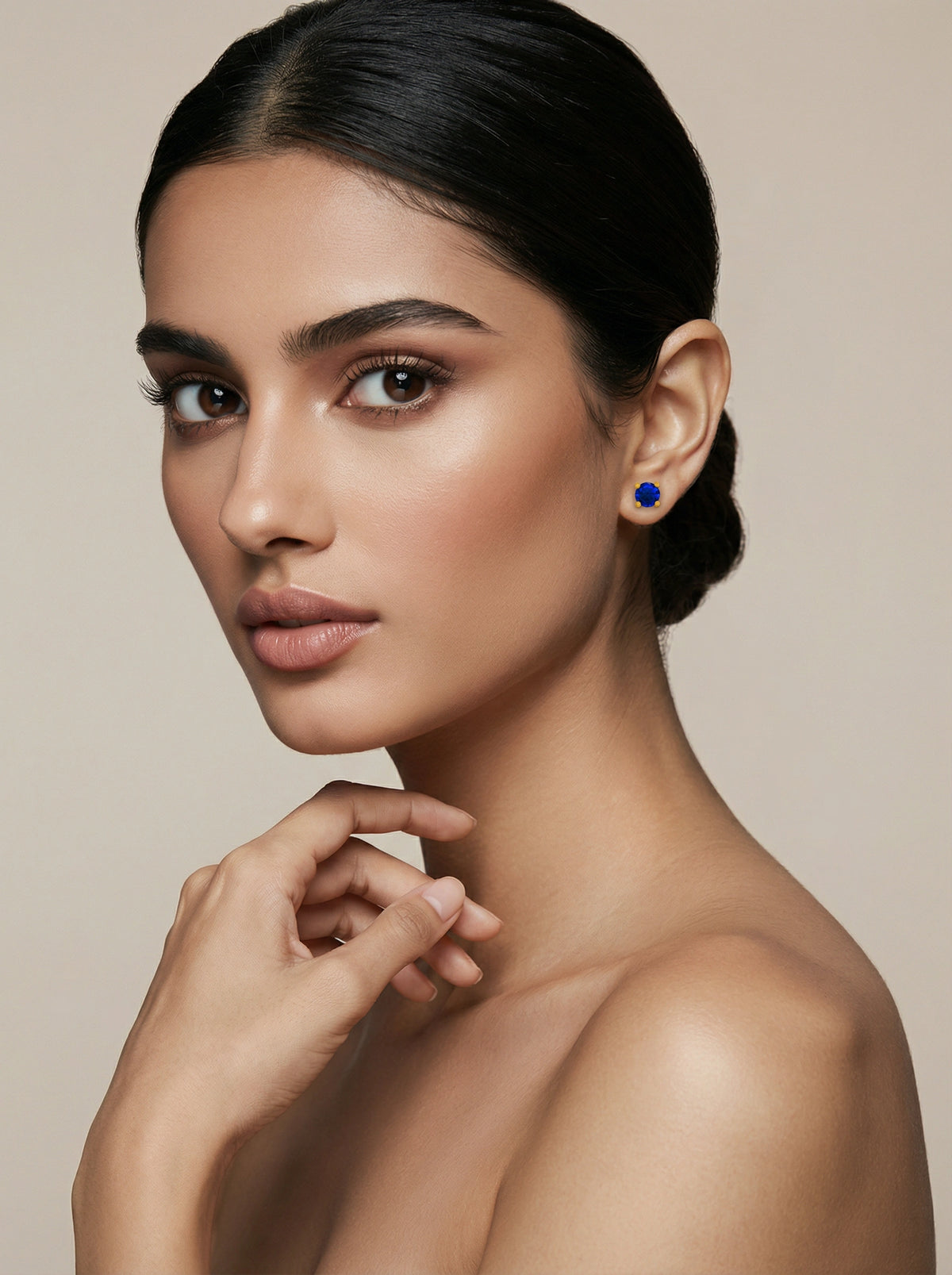 Woman wearing a blue earring 18k gold plated against a beige background