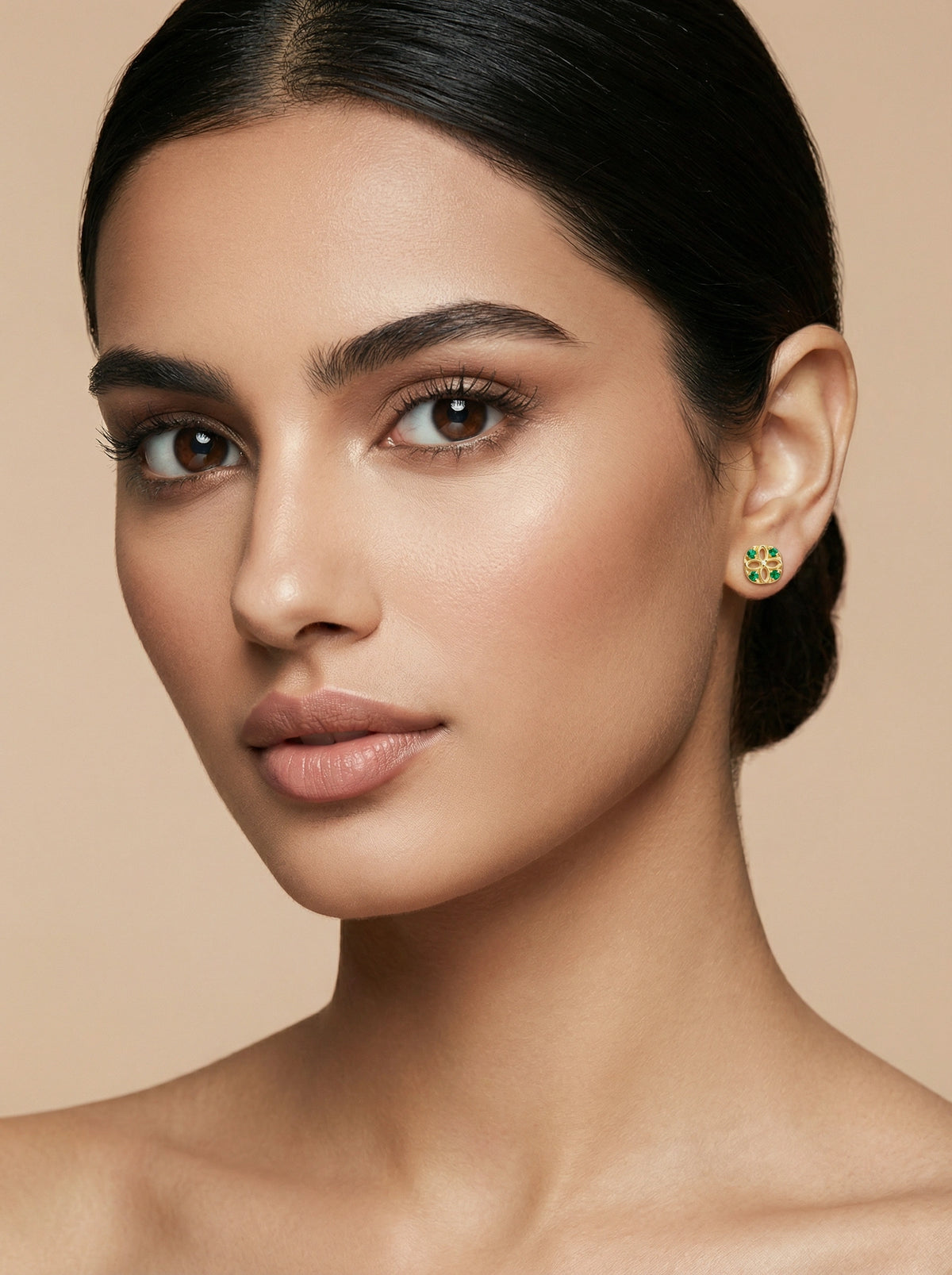 close-up of a woman wearing 18k gold plated earrings with a beige background