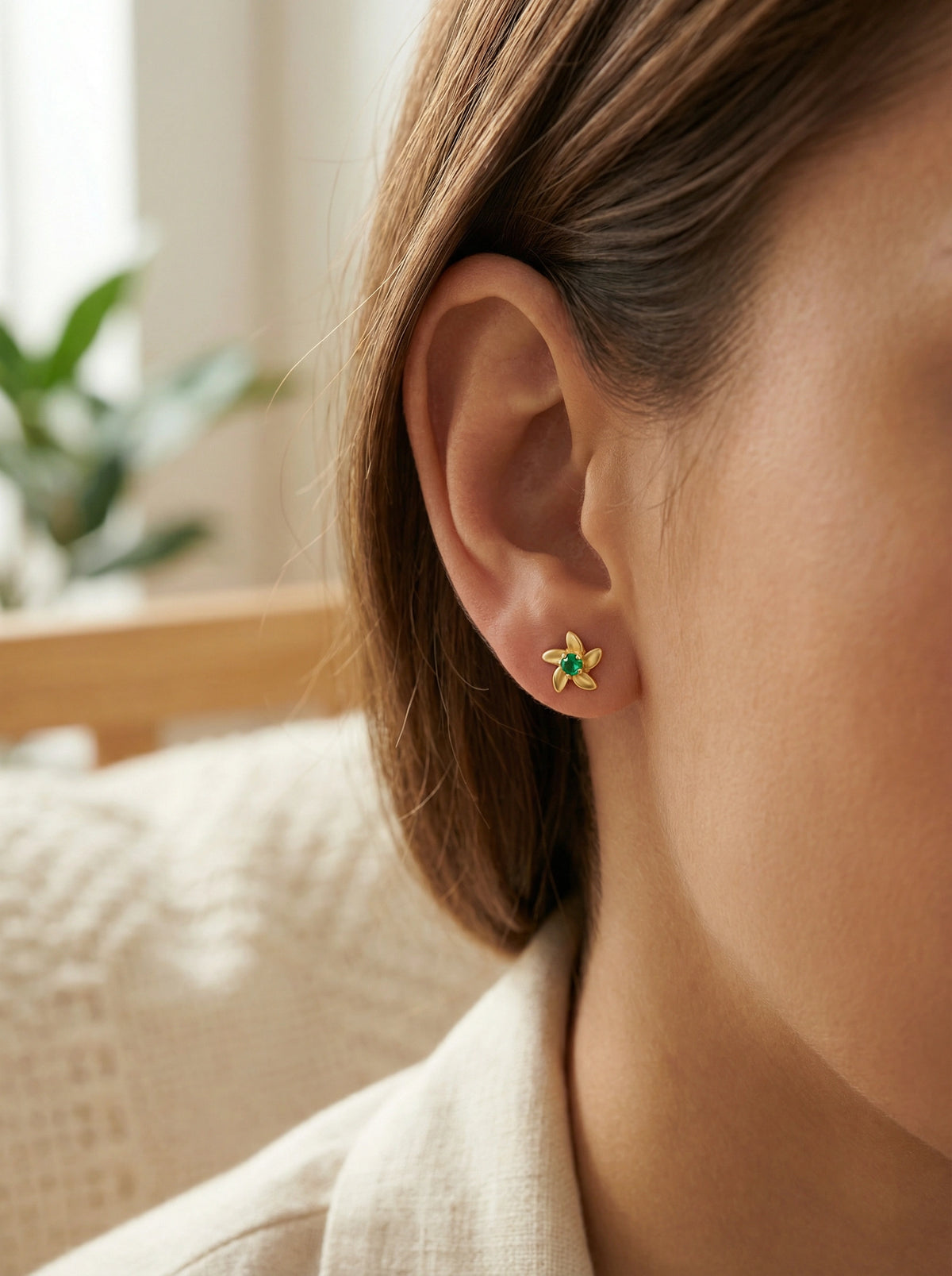 close-up of an ear wearing a green and 18k gold plated  gold earring with a blurred background