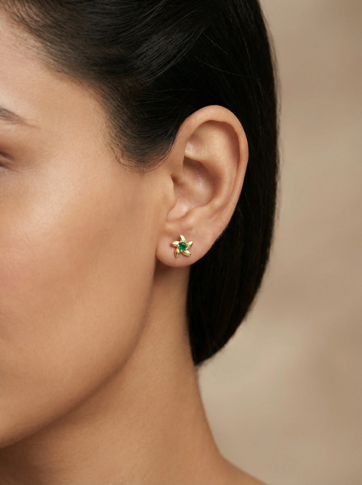 close-up of a person wearing a 18k gold plated green gemstone earring with a blurred background