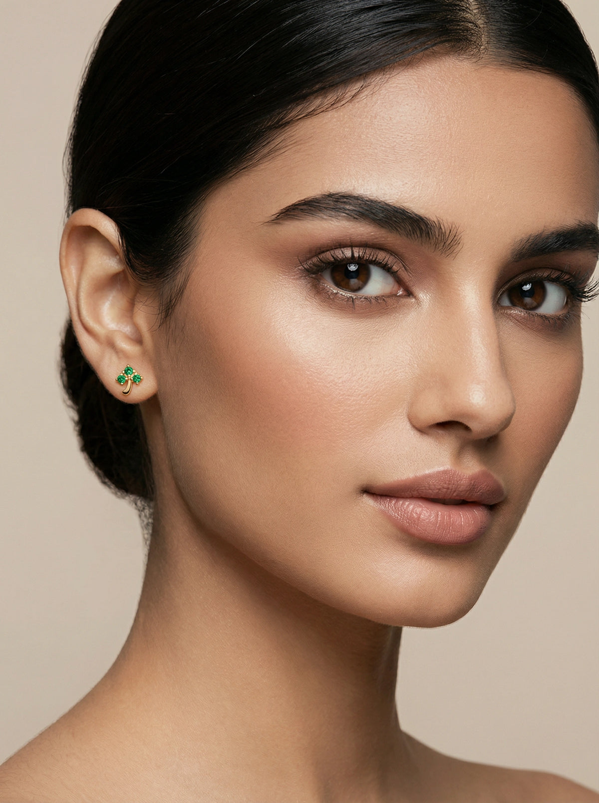 close-up of a woman wearing a green 18k gold plated earring against a beige background