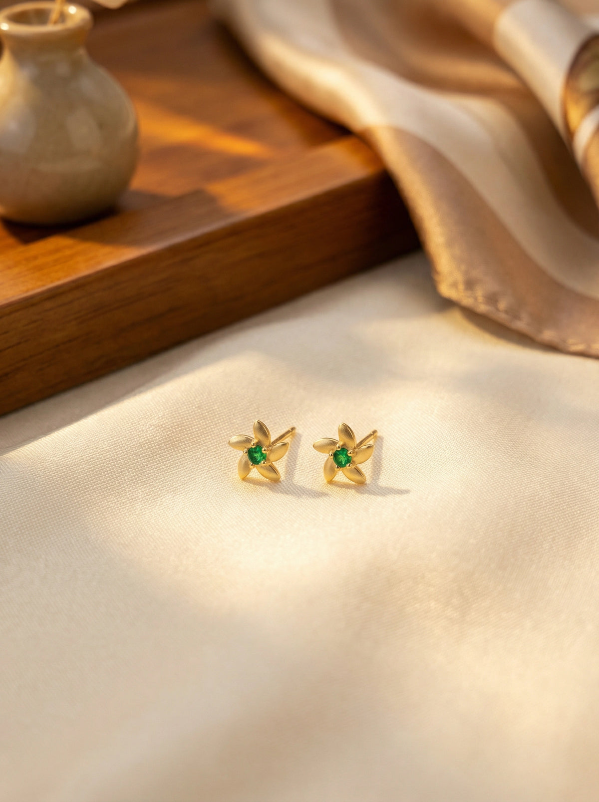 18k Gold plated earrings with green gemstones on a soft fabric background