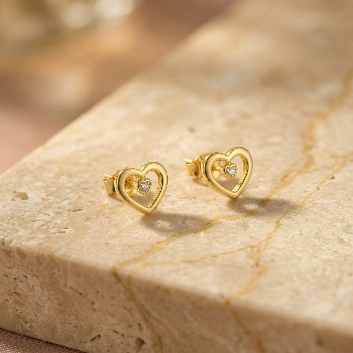 18k gold plated heart-shaped earrings with small diamonds on a beige stone surface