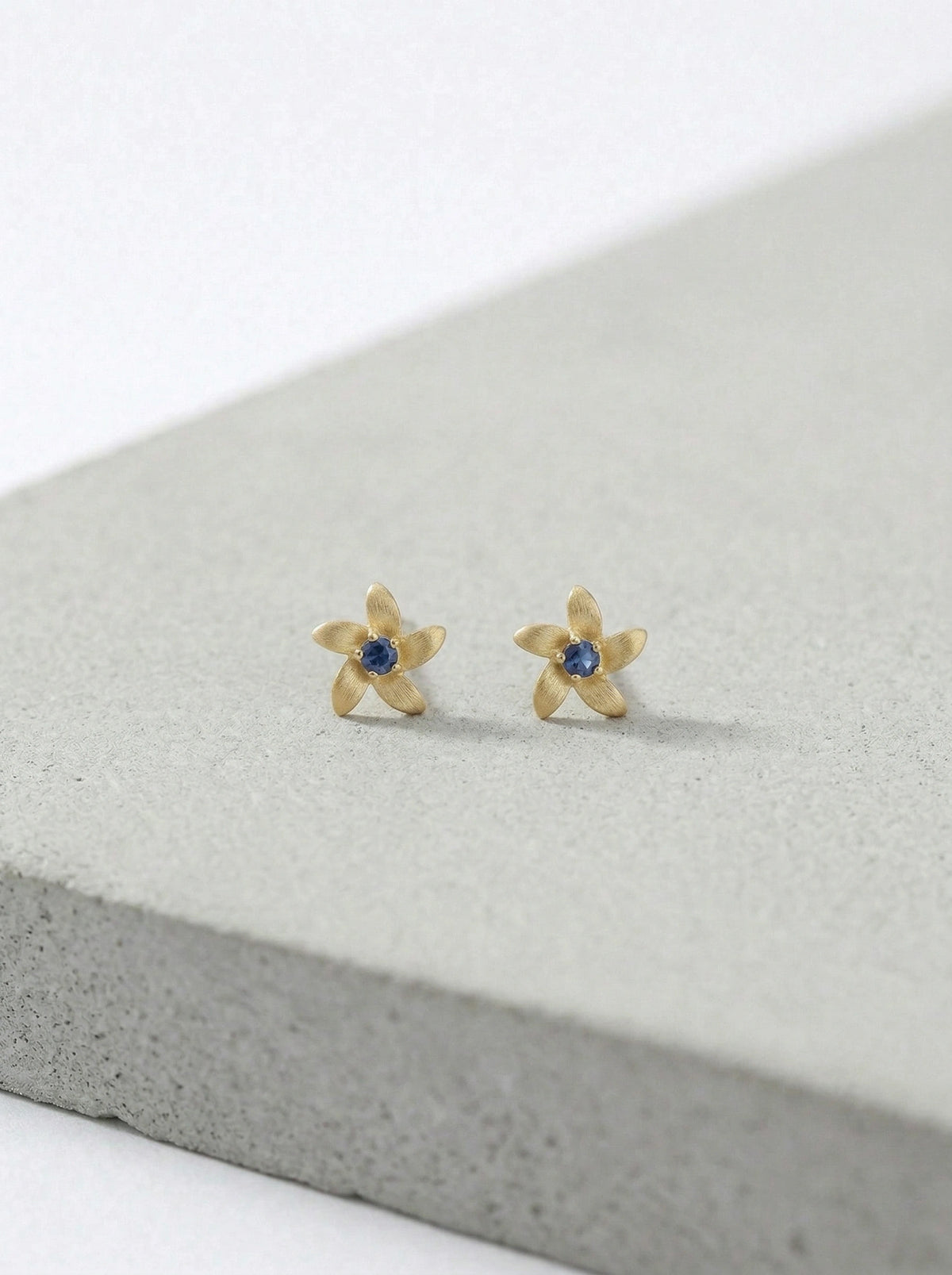 18k gold plated flower-shaped earrings with blue stones on a gray surface