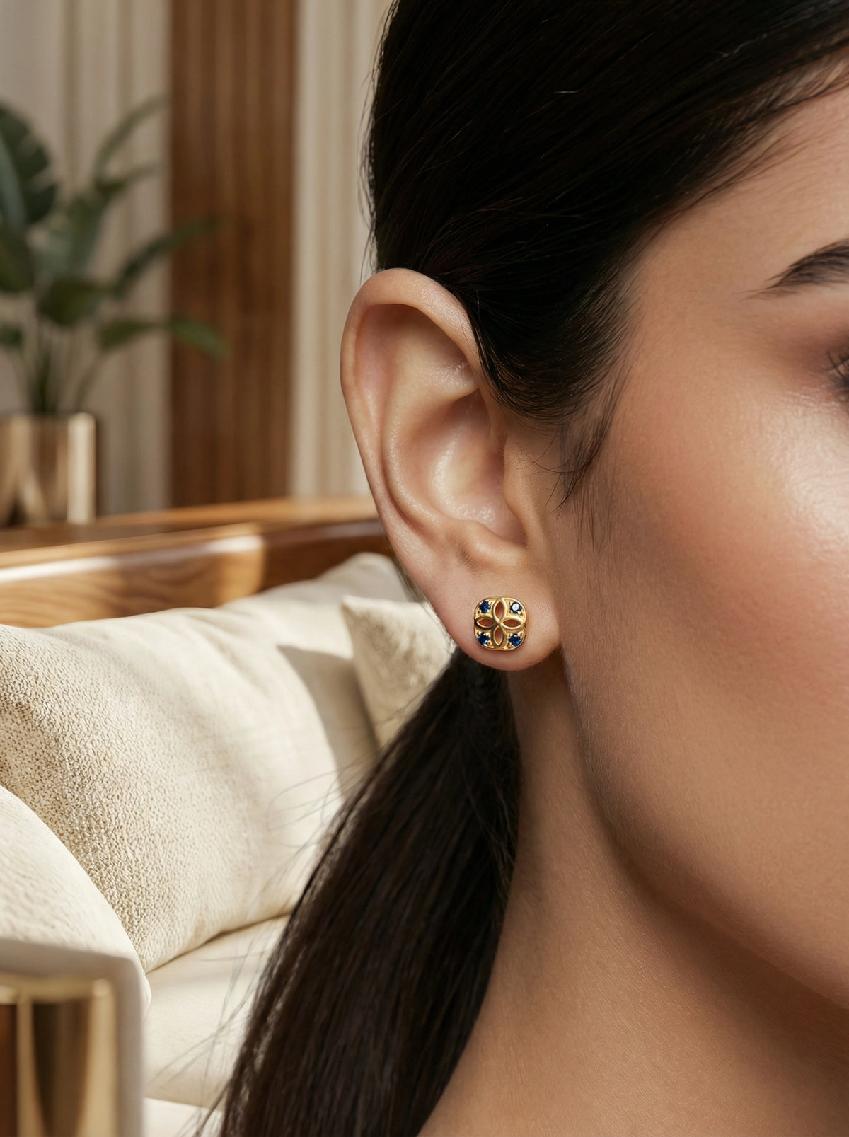 close-up of a person wearing a 18k gold plated earring with a blurred indoor background
