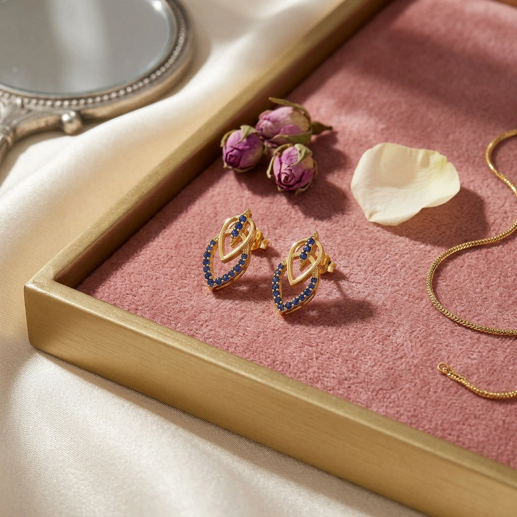 18k gold plated earrings with blue stones on a pink tray with flowers and a mirror.