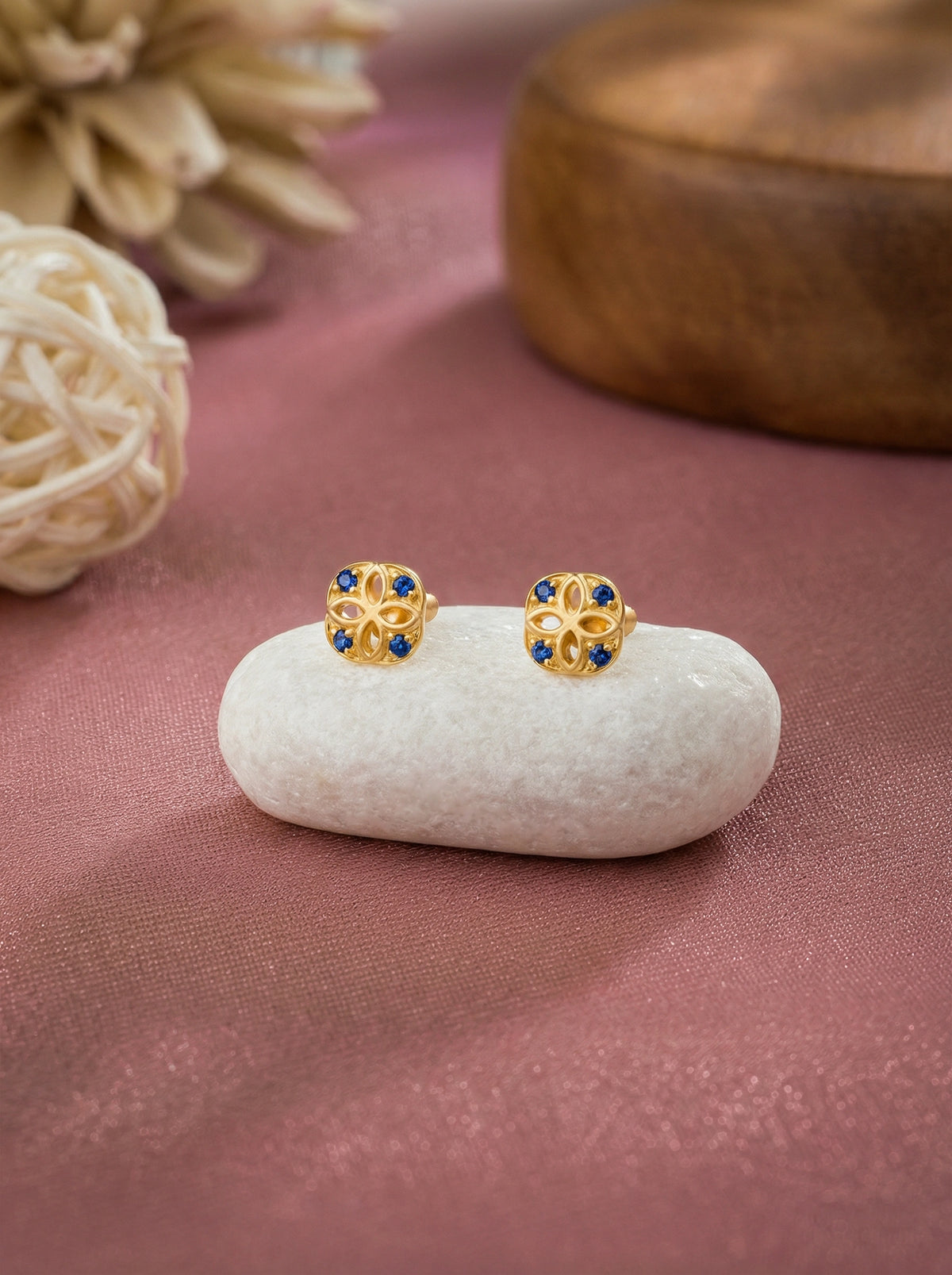 18k gold plated earrings with blue stones on a white stone with a pink fabric background