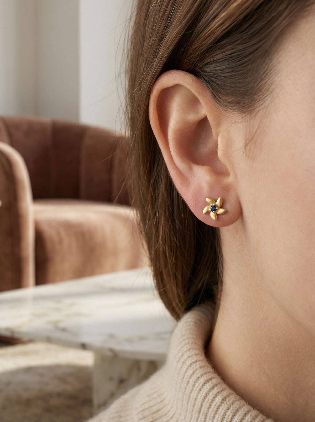 close-up of an ear wearing a 18k  gold plated  earring with a star design, blurred background