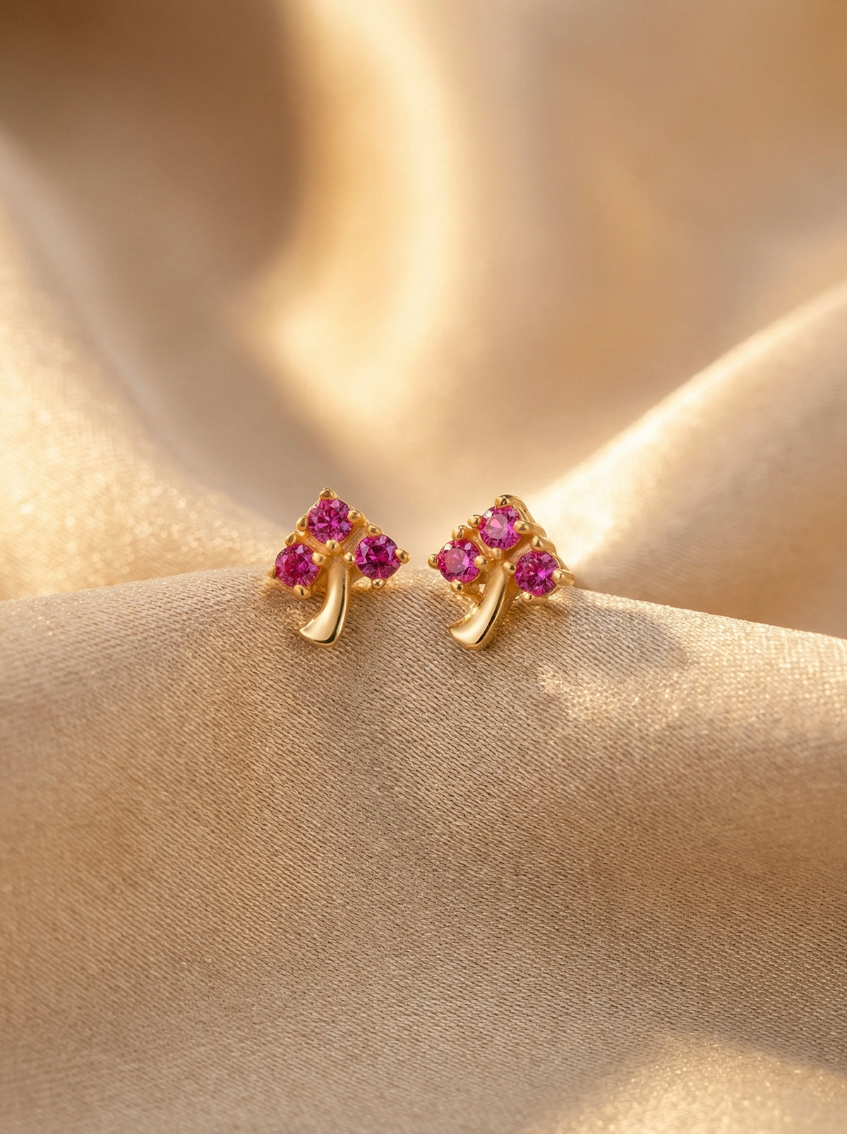 18k gold plated earrings with pink gemstones on a beige fabric background