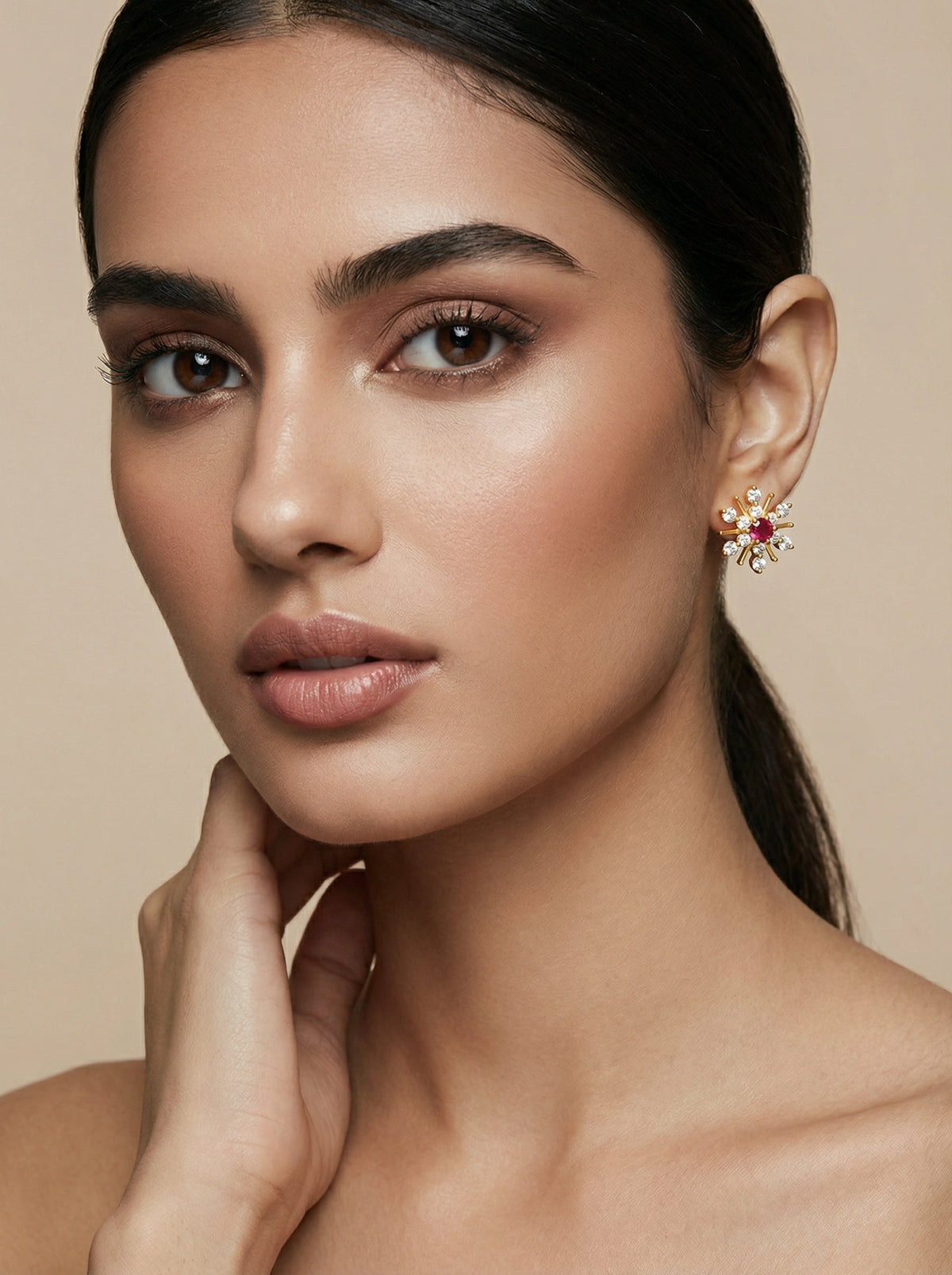 close-up of a woman wearing a floral 18k gold plated earring with a red gemstone on a beige background