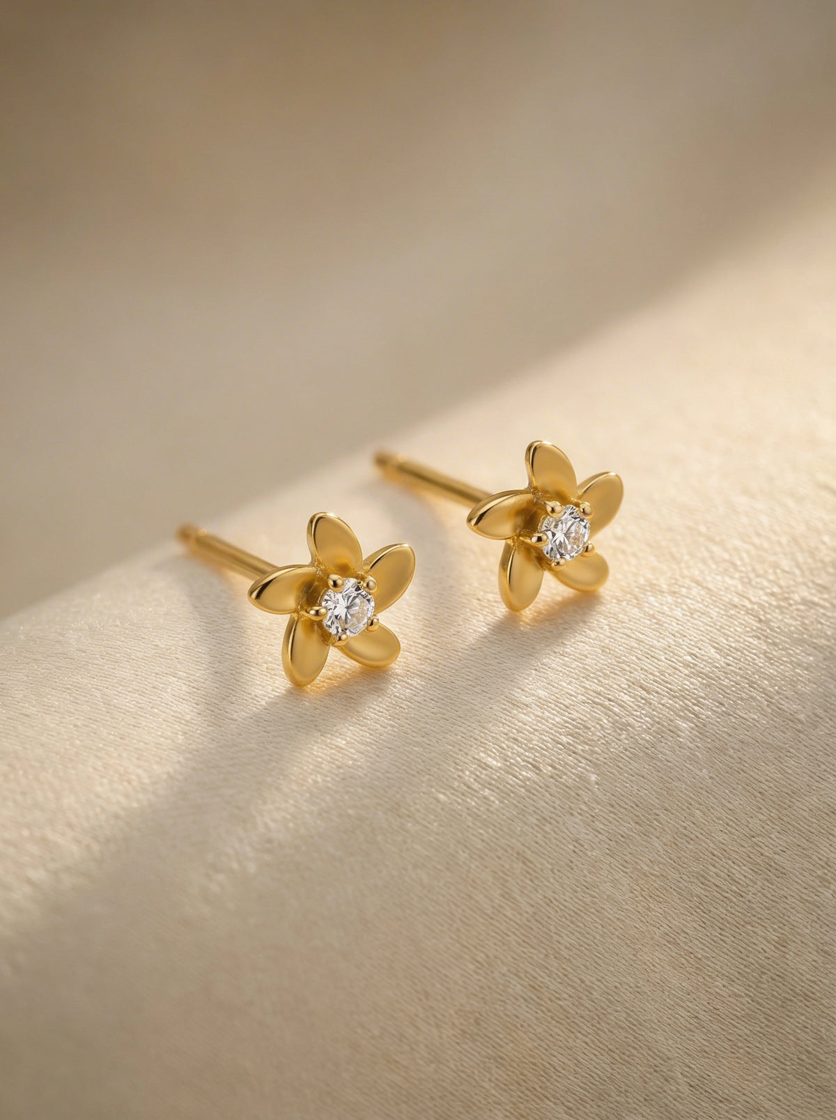  18k gold plated flower-shaped earrings with diamond centers on a gold background
