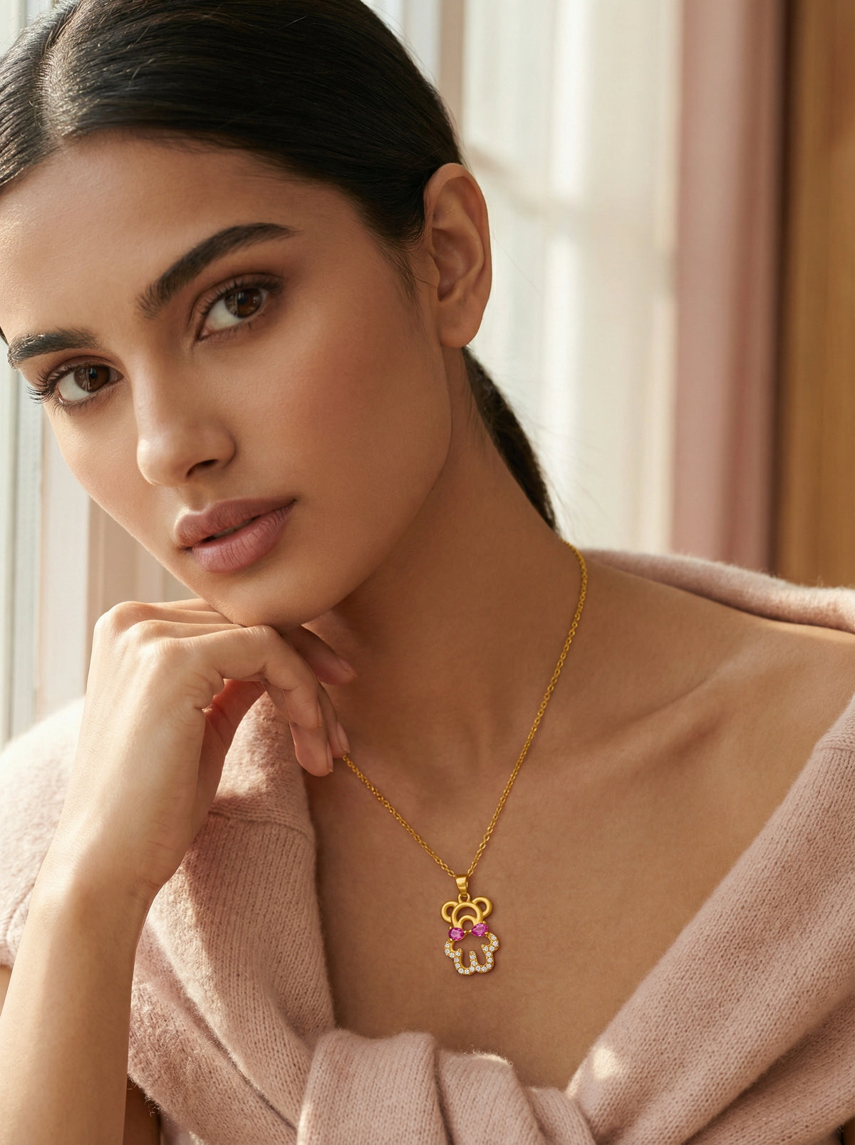 woman wearing a 18k gold plated necklace with a pink gemstone in a soft, blurred indoor setting