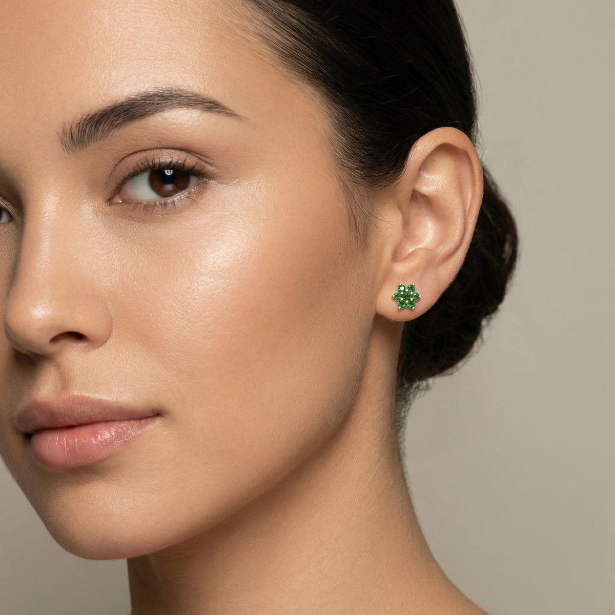 close-up of a woman wearing green 18k gold plated earrings with a neutral background