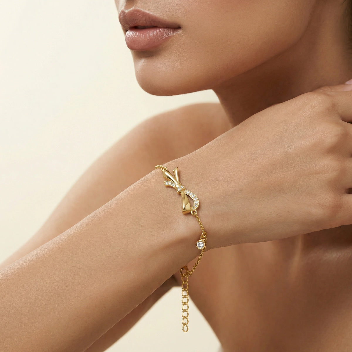 18k gold plated bracelet with a bow design on a model's wrist against a beige background