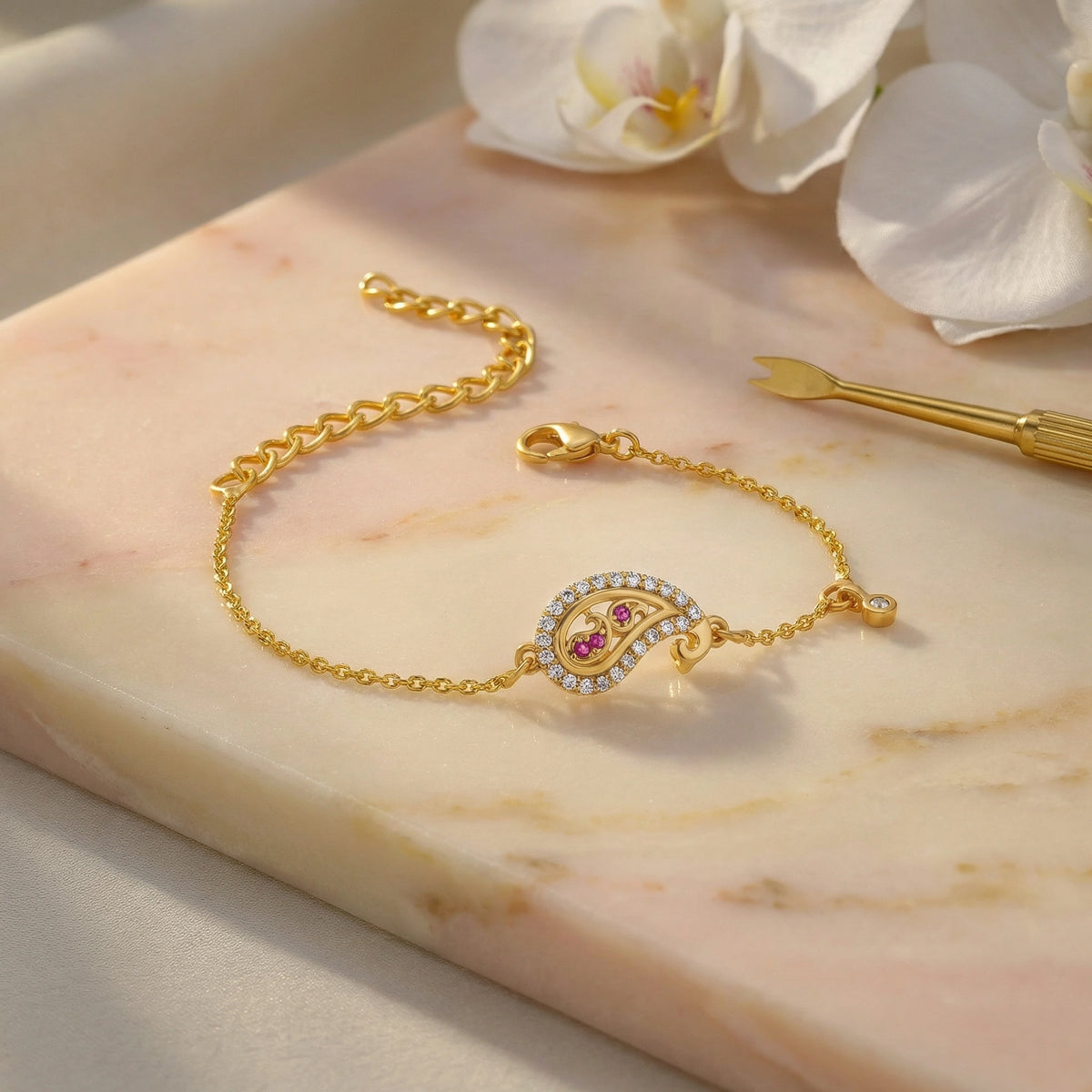 18k gold plated bracelet with a decorative clasp on a marble surface with flowers in the background