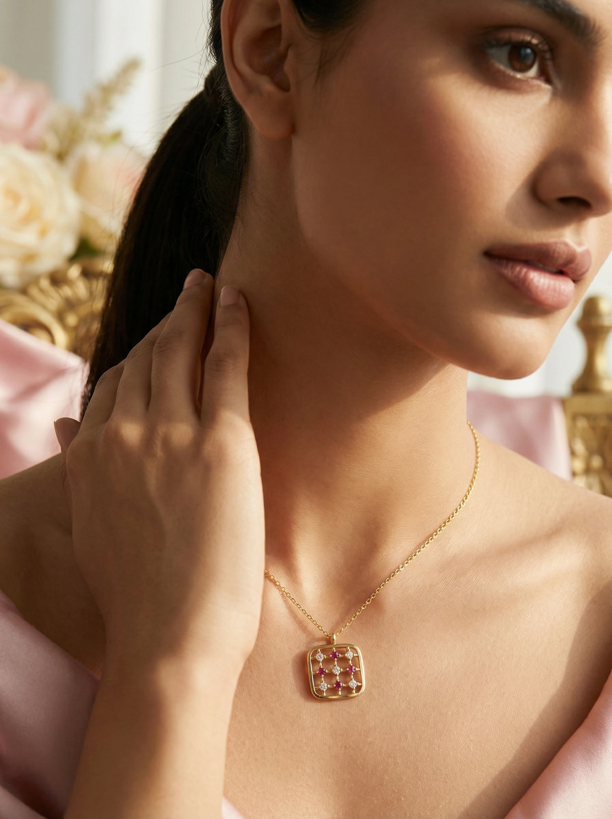 woman wearing a 18k gold plated necklace with a red gemstone pendant, touching her neck.