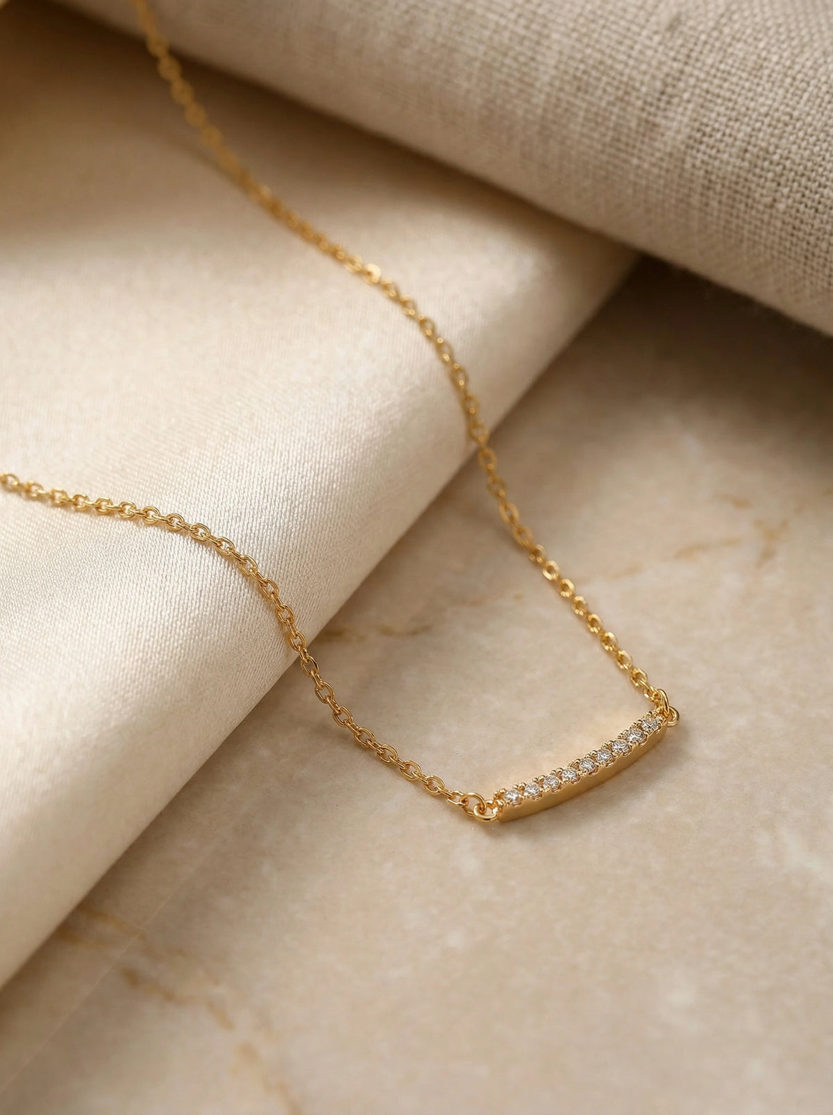 18k gold plated necklace with small diamonds on a beige fabric background