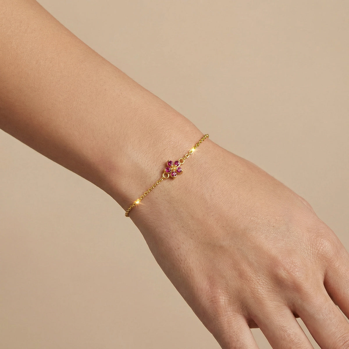 18k gold plaetd bracelet with a floral design on a wrist against a beige background