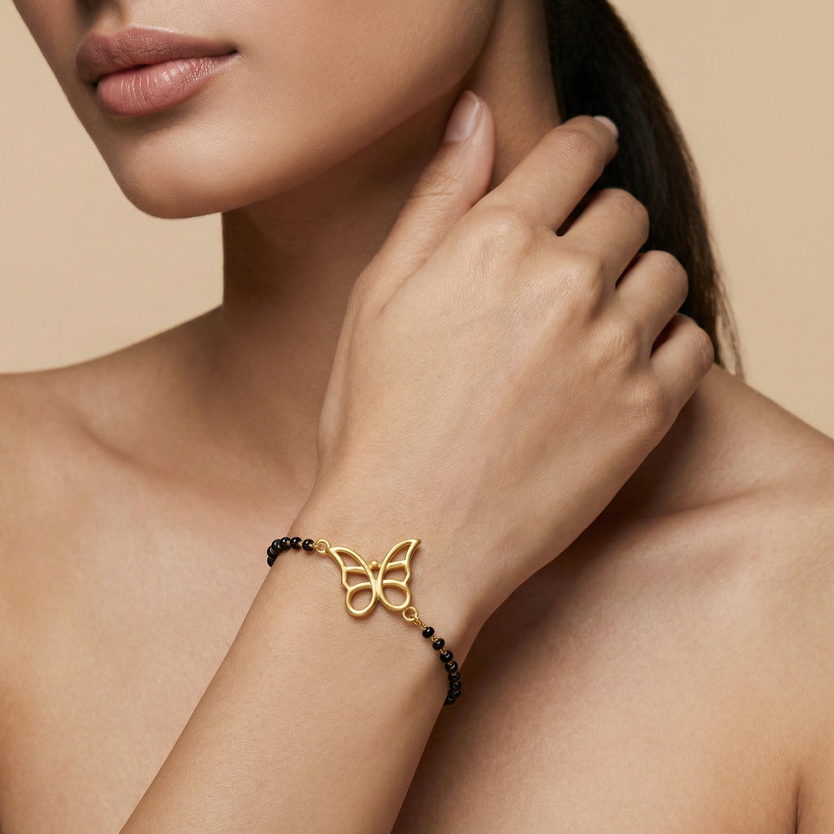 18k gold plated butterfly bracelet with black beads on a woman's wrist against a beige background