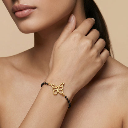 18k Gold plated butterfly bracelet with black beads on a woman's wrist against a beige background