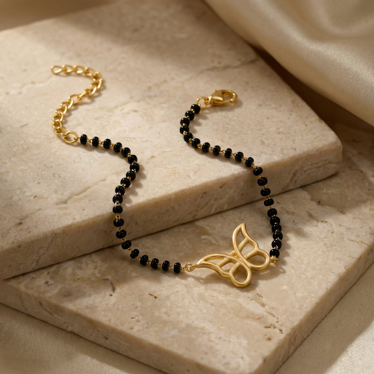 Black beaded bracelet with 18k gold plated clasp and decorative element on a marble surface
