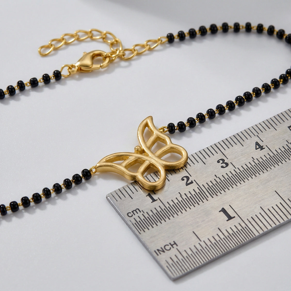 18k gold plated  butterfly pendant on a black beaded chain with a ruler for scale on a light gray background