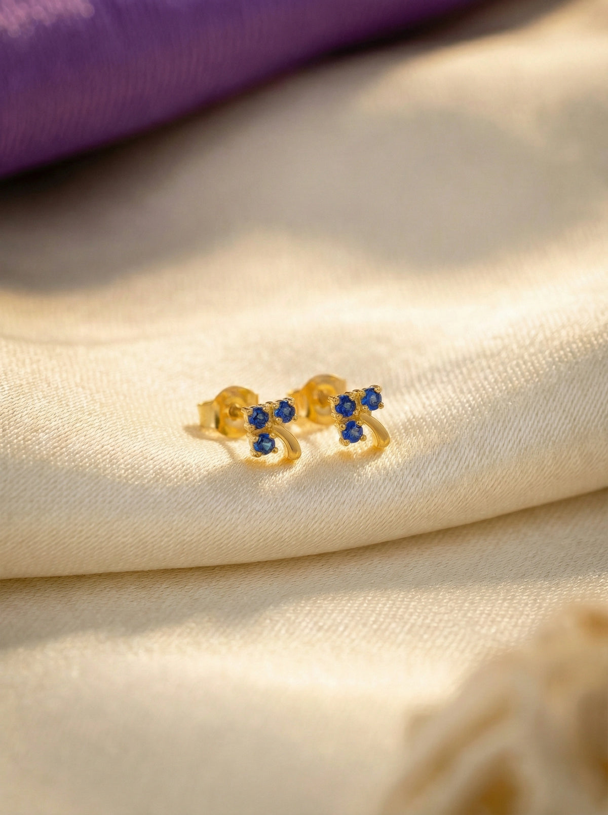 18k gold plated  bow-shaped earring with blue stones on a beige fabric background