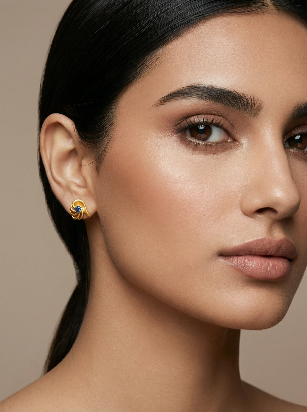 close-up of a woman wearing a 18k gold plated earring against a neutral background