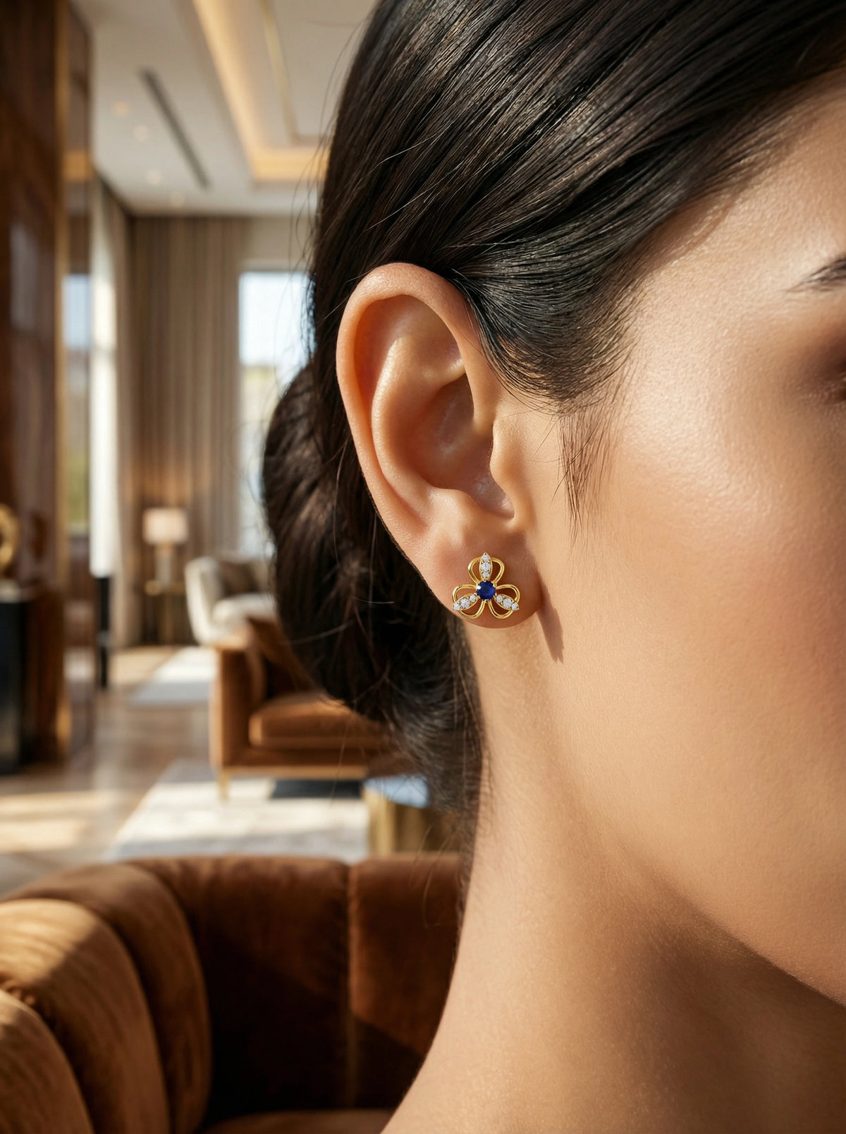 close-up of a person wearing a 18k gold plated earring with a blue gemstone in an indoor setting.