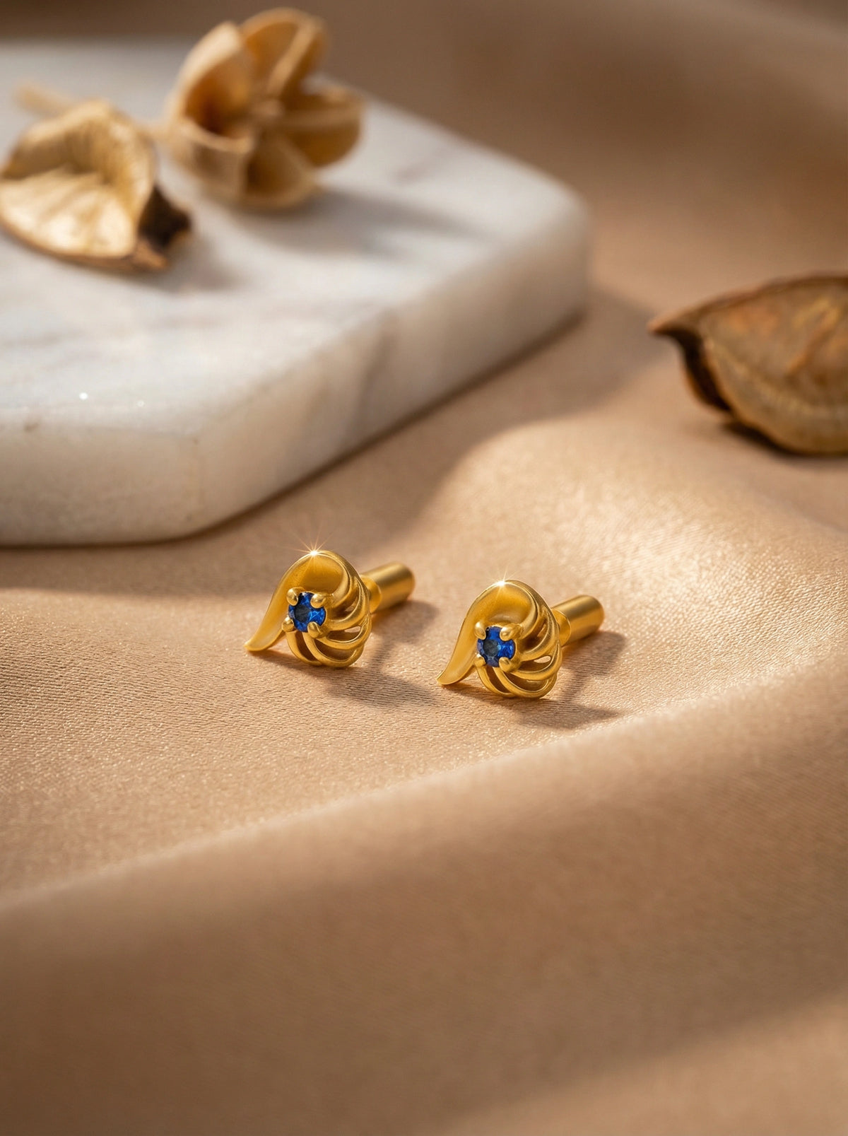 18k gold plated earrings with blue stones on a beige surface