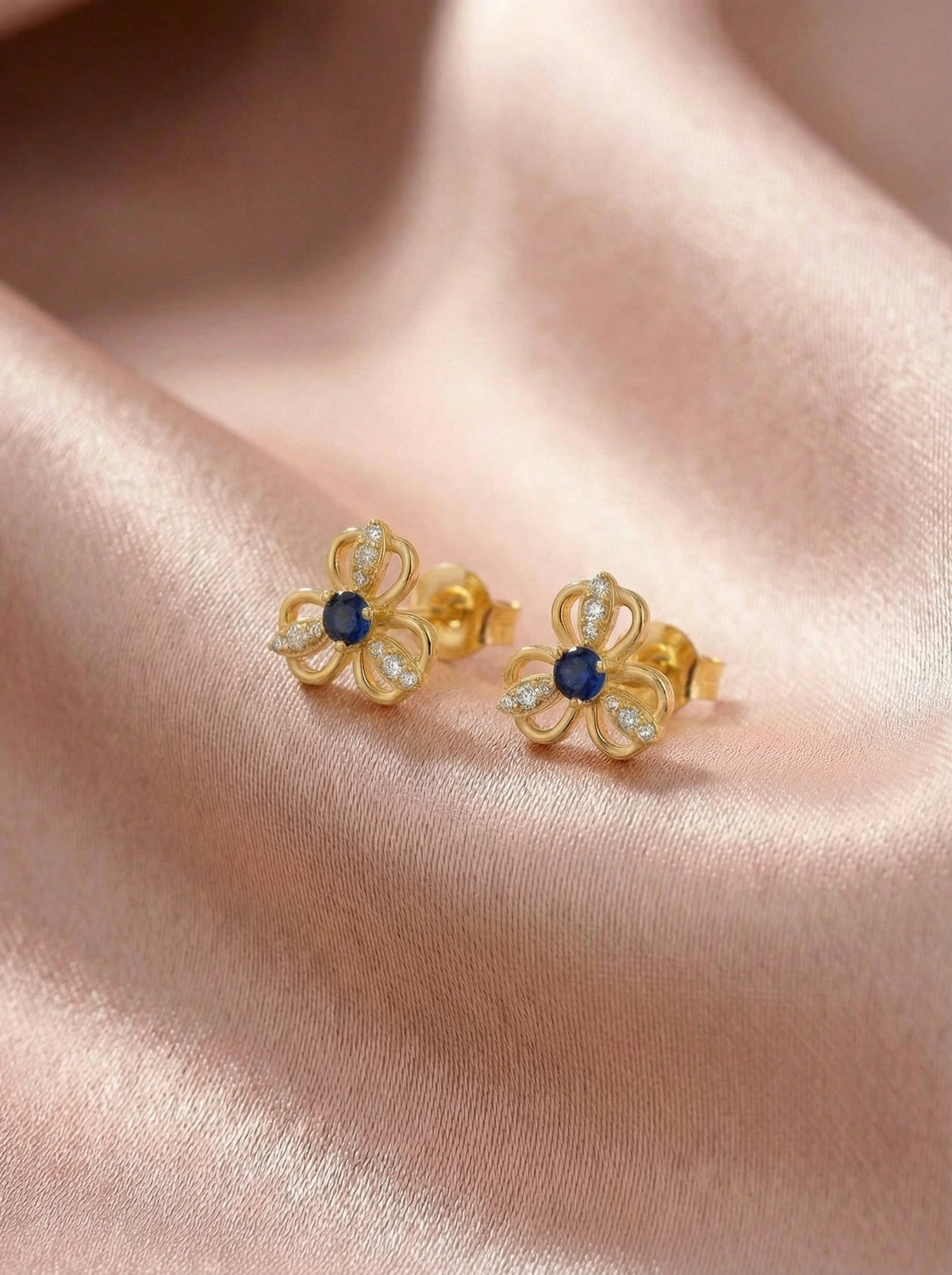 18k gold plated flower-shaped earrings with blue centers on a pink fabric background