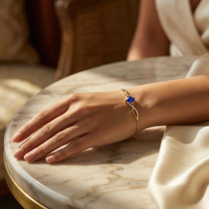 Hand wearing a 18k gold plated  bracelet with a blue stone on a marble surface